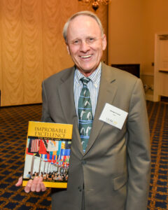 George La Noue holds his book Improbable Excellence at a reception for UMBC alumni in Annapolis.