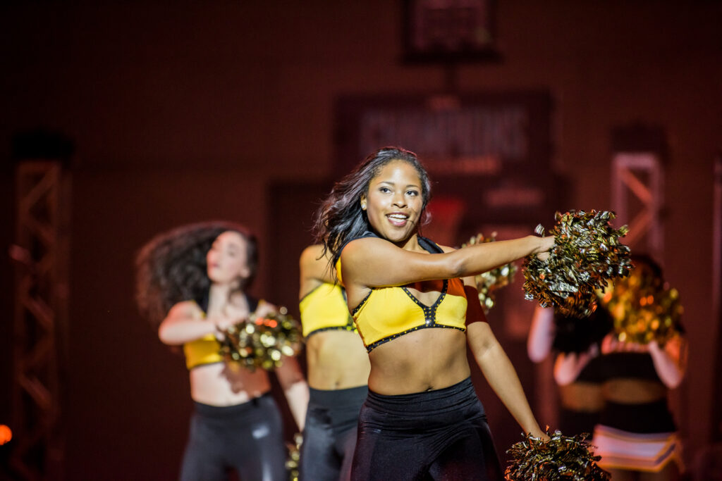 Three dancers in black and gold uniforms cheer.