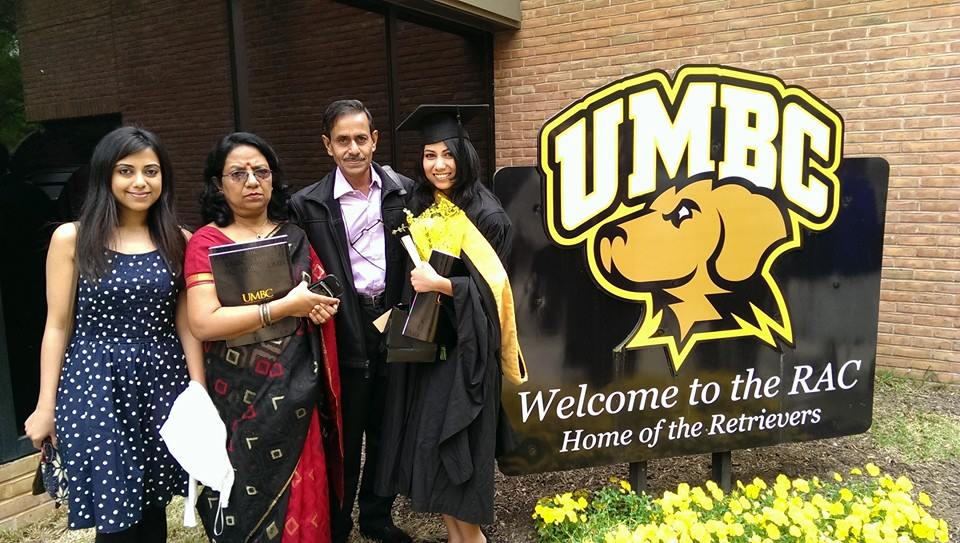 A student in graduation clothing poses with parents and sister by UMBC sign.