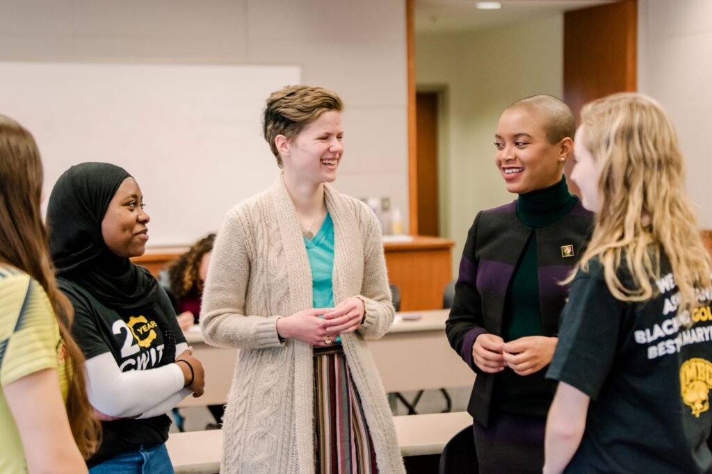 Five women in conversation, smiling. One wears a shirt with UMBC logo. Another's shirt says 20 Years CWIT.